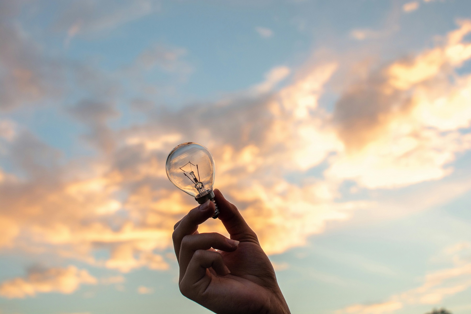 Individual showcasing light bulb with cloudy sky backdrop, representing inspiration